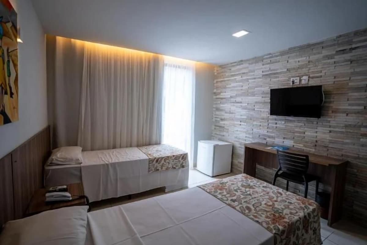 Habitación de hotel con dos camas, un escritorio, un televisor y una ventana con cortinas.