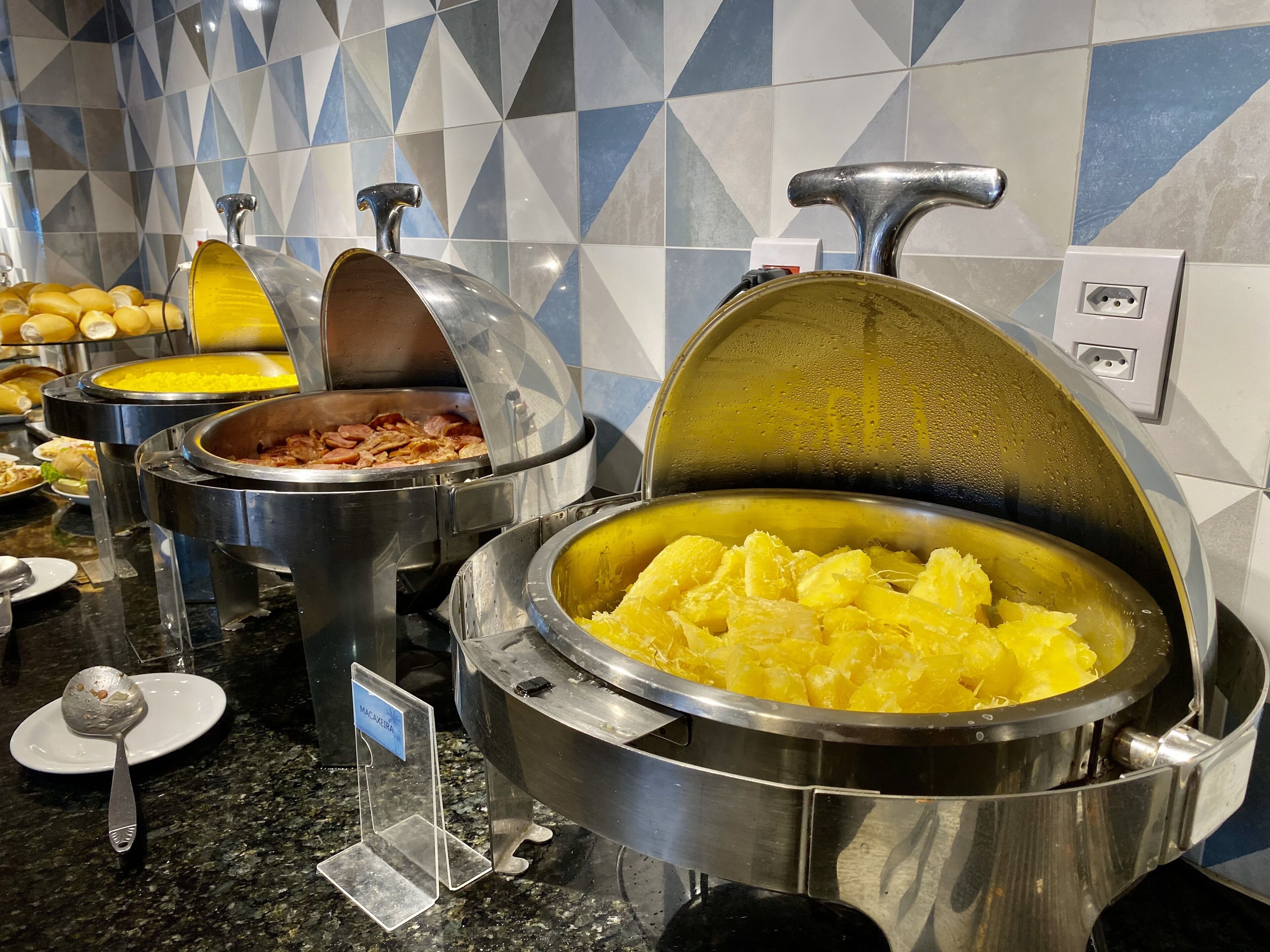 Un buffet proposant une variété de plats, notamment un grand plat de purée de pommes de terre, un bol d’œufs brouillés et un récipient contenant des tranches de bananes.