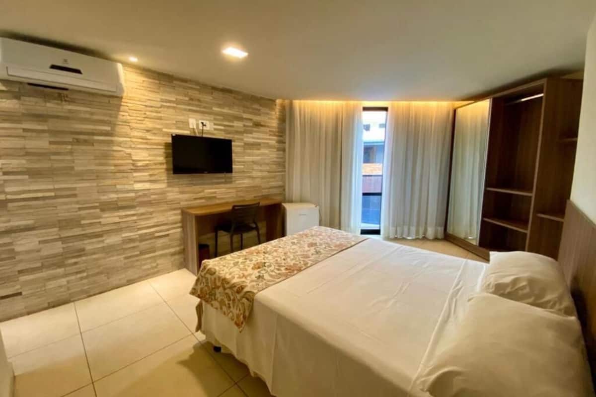 Una camera d'albergo con un letto, una scrivania, una TV a parete e un armadio.