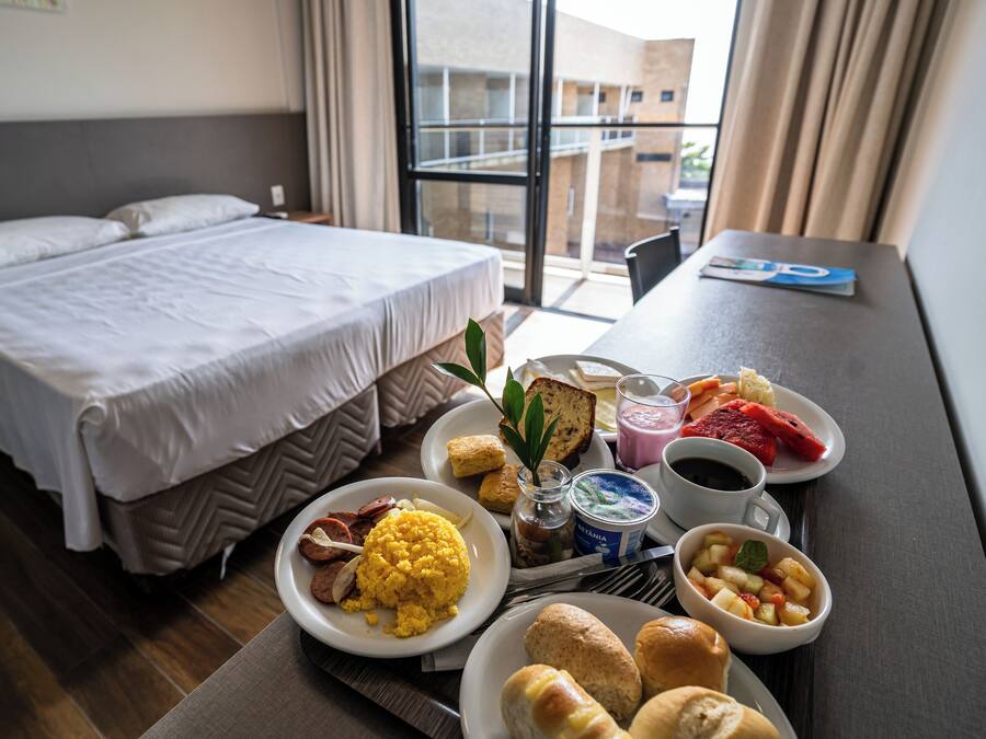 Habitació d'hotel amb un llit, safata de matí amb ous, torrades, fruita i cafè.