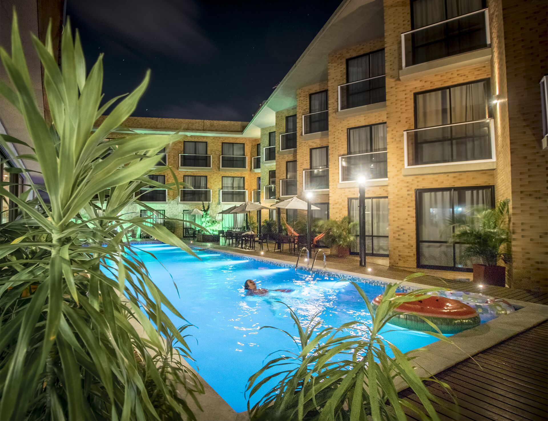 Zona de piscina con una persona nadando, rodeada por un edificio de varios pisos con balcones y ventanas.