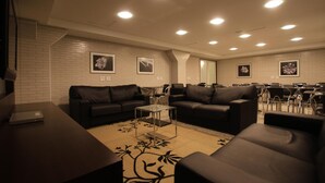 Un salon moderne avec des canapés en cuir noir, une table basse en verre et un mur en briques blanches orné de tableaux encadrés.
