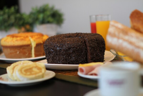 A breakfast table with a chocolate cake, a muffin, a plate with ham, and a glass of orange juice.