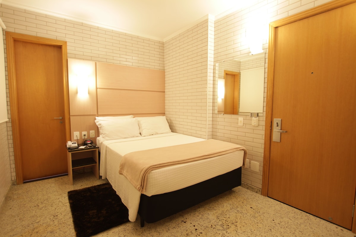 A hotel room with a bed, nightstand, and a wooden door.