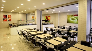 Un comedor amplio con varias mesas y sillas, una barra central con exhibición de alimentos y paredes decoradas con motivos frutales.