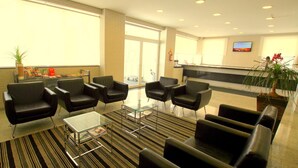 Un vestíbulo de hotel con sillones de cuero negro, una mesa de centro de vidrio y una recepción.