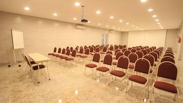 Un salón de conferencias con filas de sillas, una pizarra y un proyector en el techo.