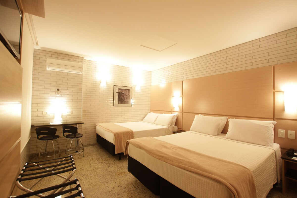 A hotel room with two beds, a desk with chairs, and a small seating area.