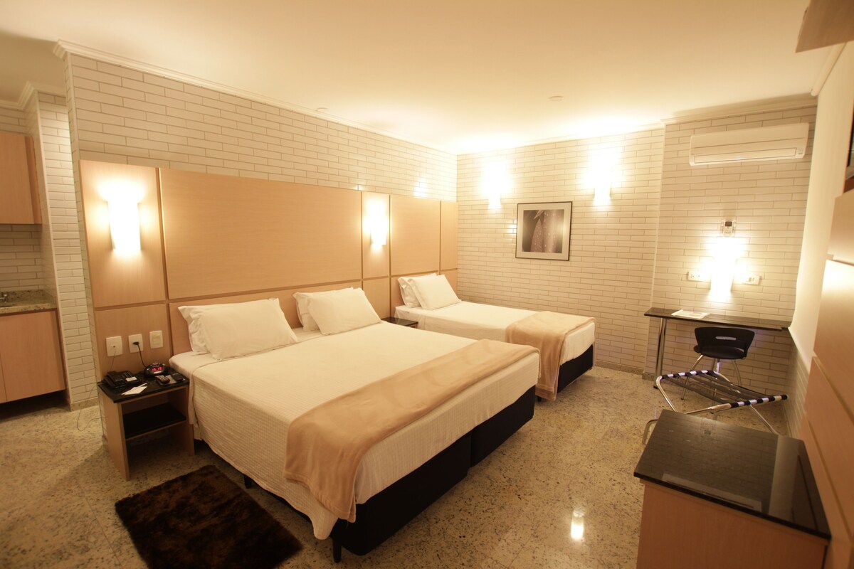 A hotel room with two beds, a desk, a chair, a small table, and a mirror.