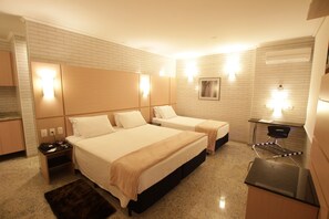 A hotel room with two beds, a desk, a chair, a small table, and a mirror.
