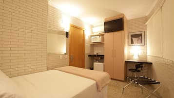 A hotel room with two beds, a microwave, a small kitchenette, and a TV mounted on the wall.