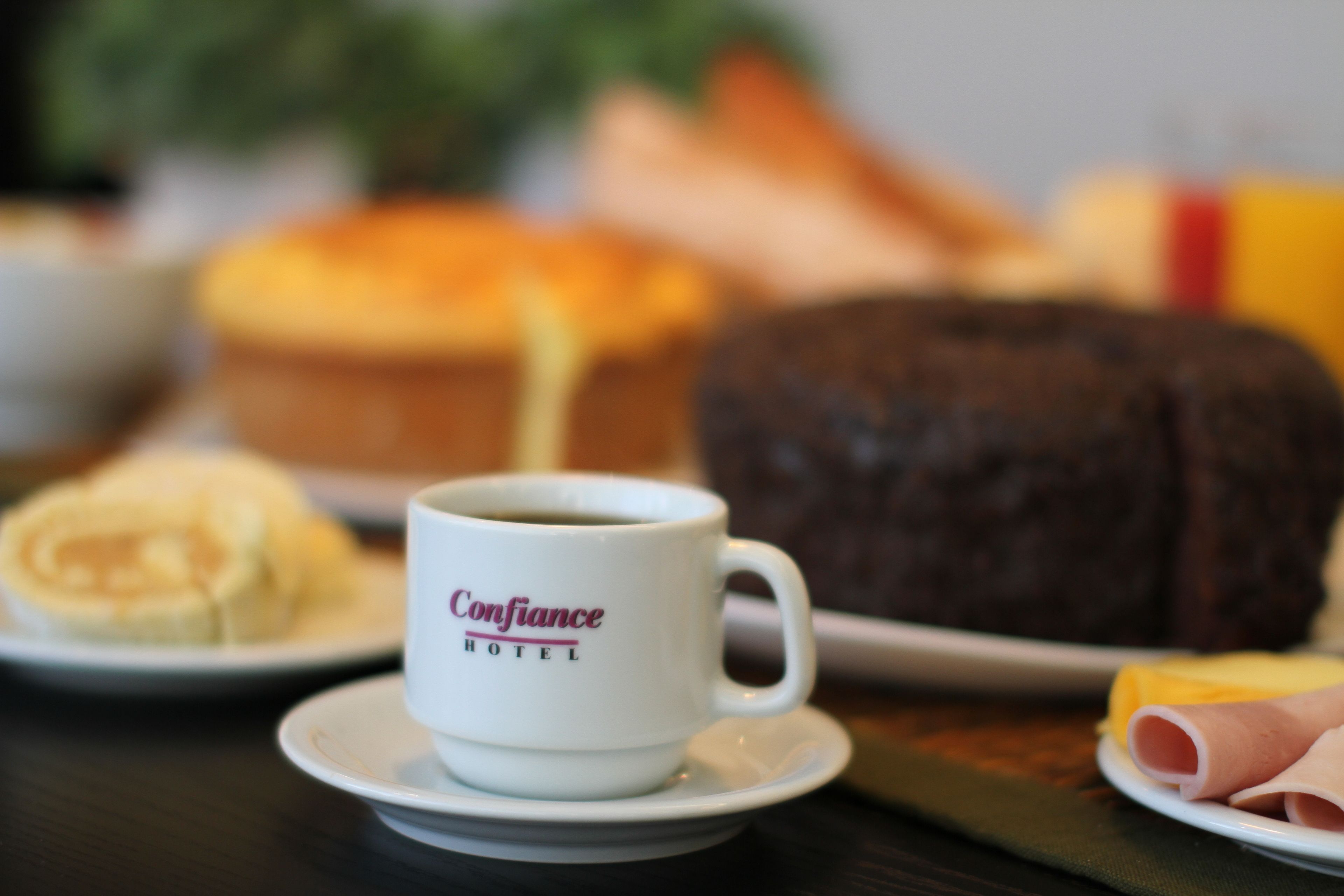 A breakfast setting with a coffee cup labeled "Confidence Hotel" and various food items on plates.