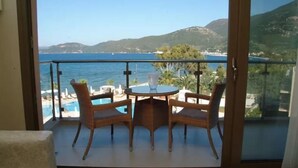 En balkon med fletstole og et bord, med udsigt over en pool og en smuk kystlinje.
