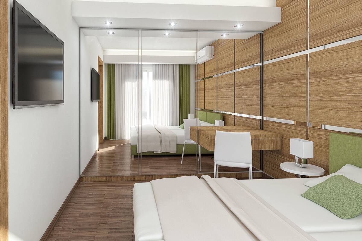 Moderni hotellihuone, jossa on puulattia, sänky, työpöytä tuolilla, televisio ja suuri peili.