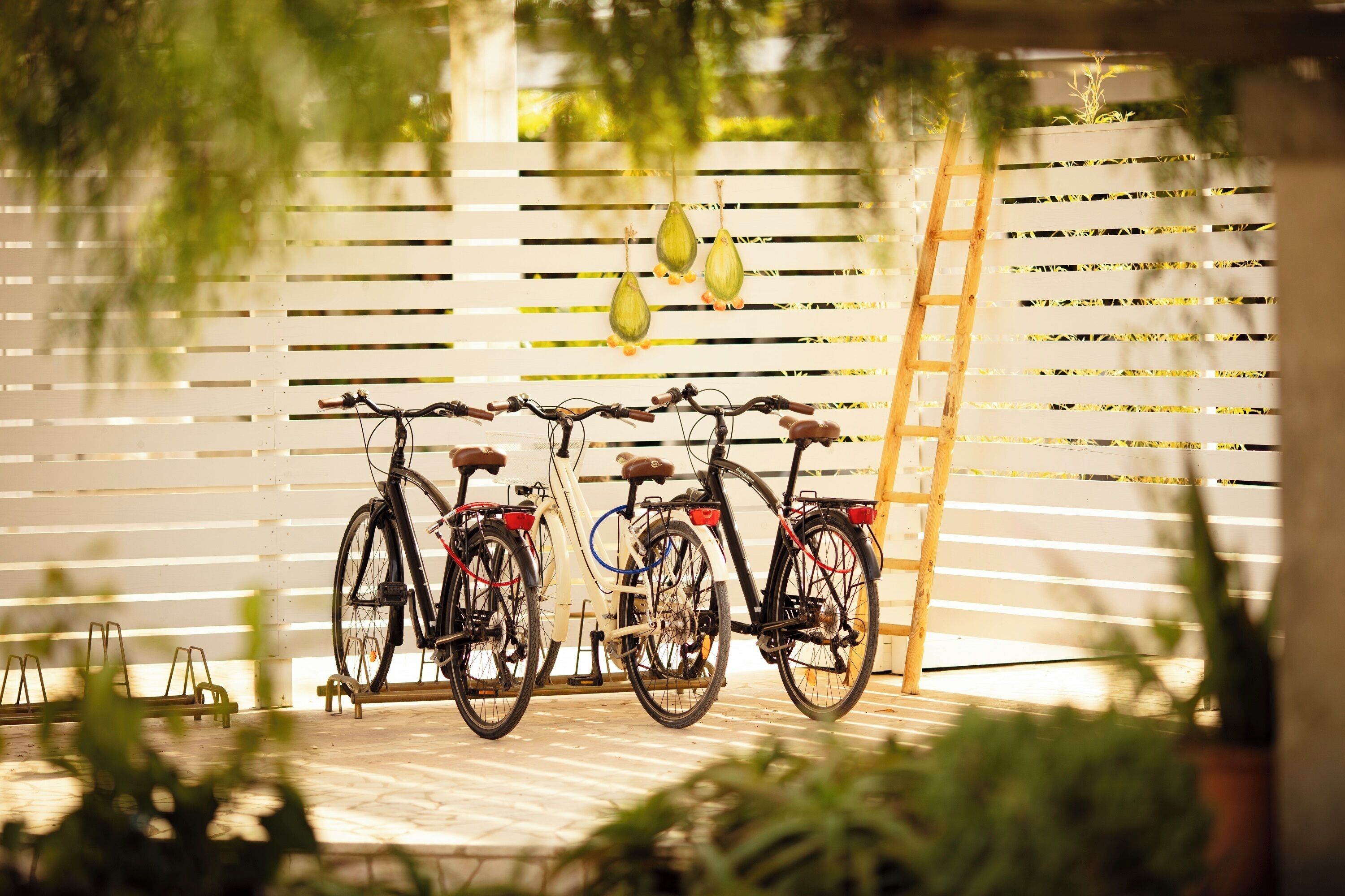 Deux vélos sont garés contre une clôture blanche à lattes, ornée d’éléments décoratifs suspendus.