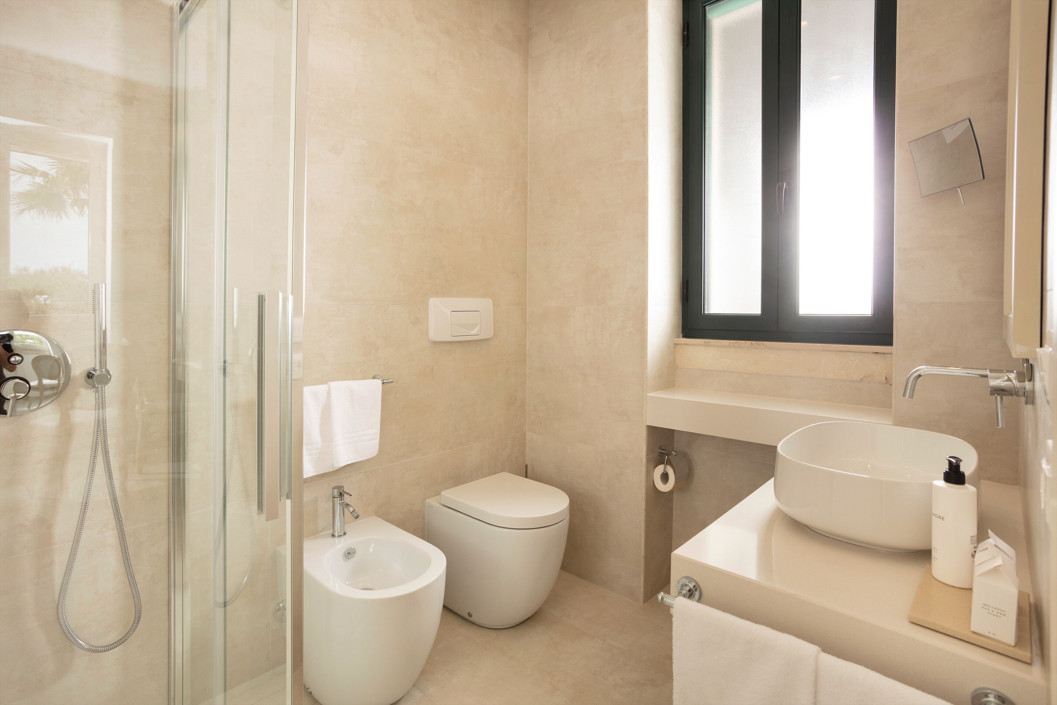 Un baño moderno con ducha envuelta en vidrio, un bidé, un inodoro y un lavabo con espejo sobre él.