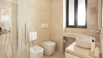 Un baño moderno con ducha envuelta en vidrio, un bidé, un inodoro y un lavabo con espejo sobre él.