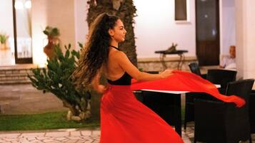 A woman in a red dress dancing outdoors, with a palm tree and a building in the background.