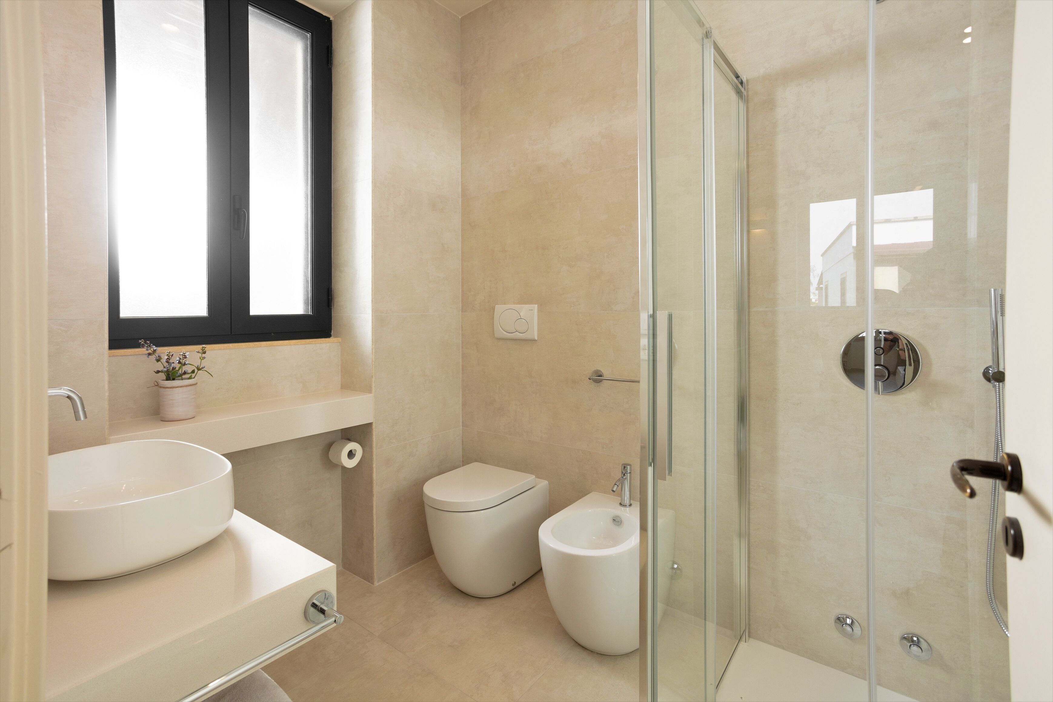 Un bagno moderno con un lavandino ampio, un water, un bidet e una cabina doccia in vetro.