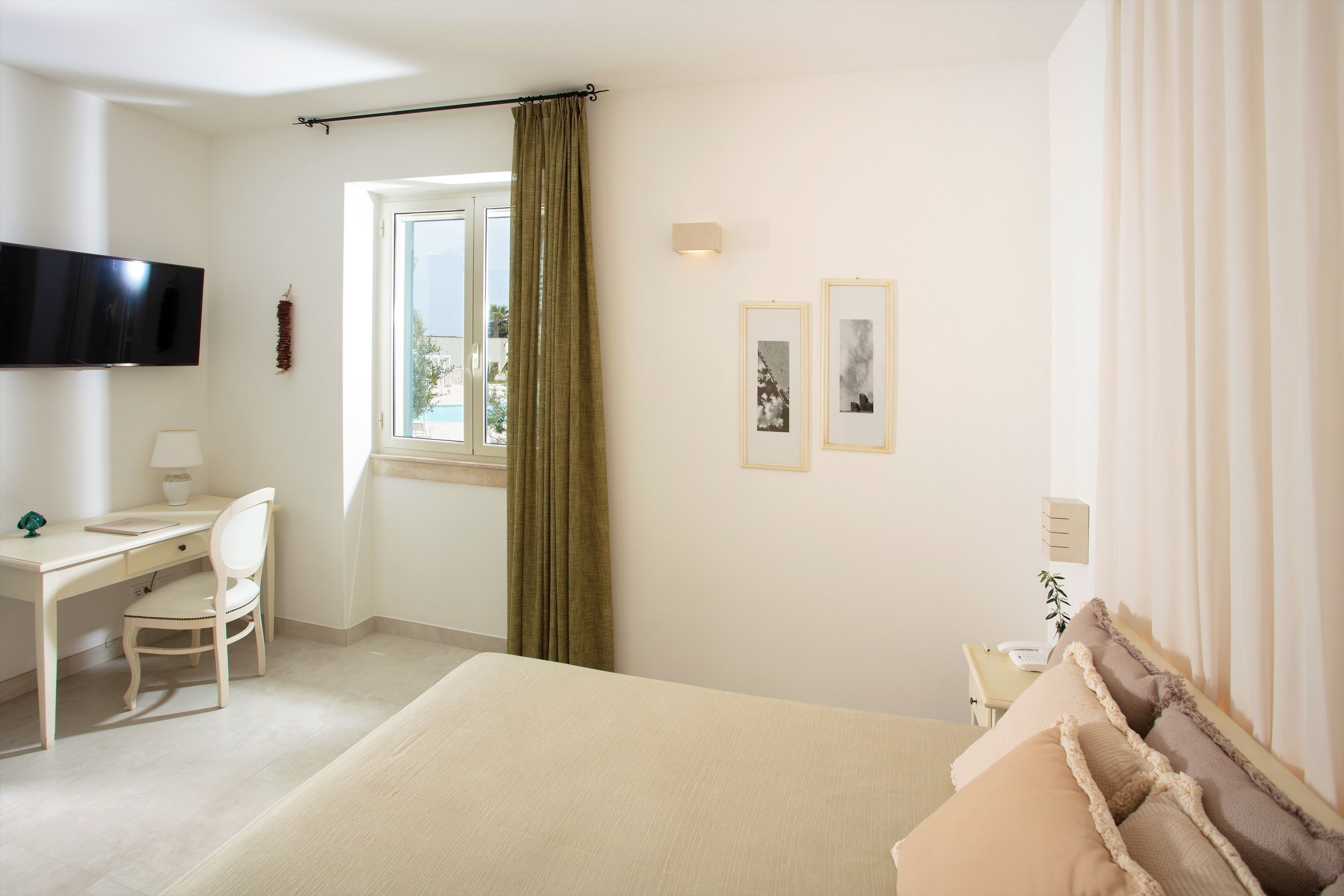 Ein Hotelzimmer mit Bett, Schreibtisch, Stuhl, Fernseher und einem Fenster mit Vorhängen.