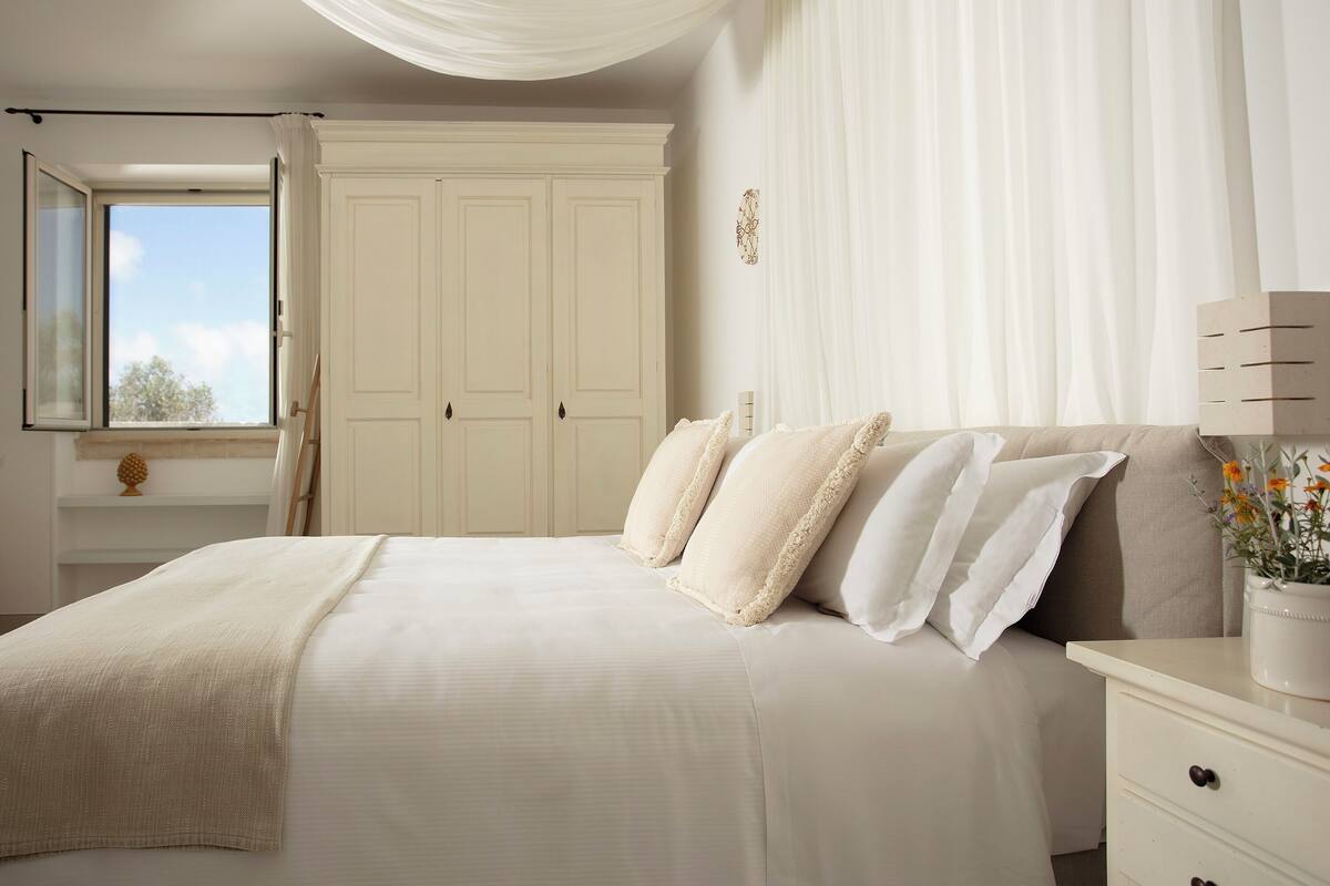 A bedroom with a large bed, a nightstand, a window with curtains, and a wardrobe.