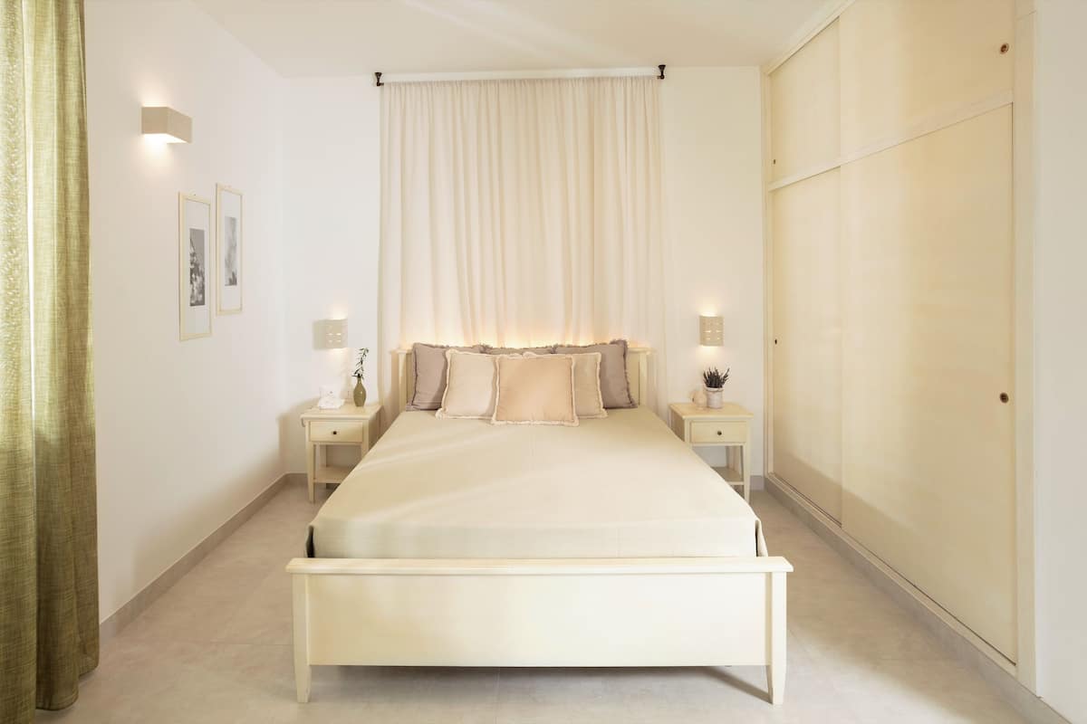 A bedroom with a bed, nightstands, a bedside table, a wardrobe, and a curtain.