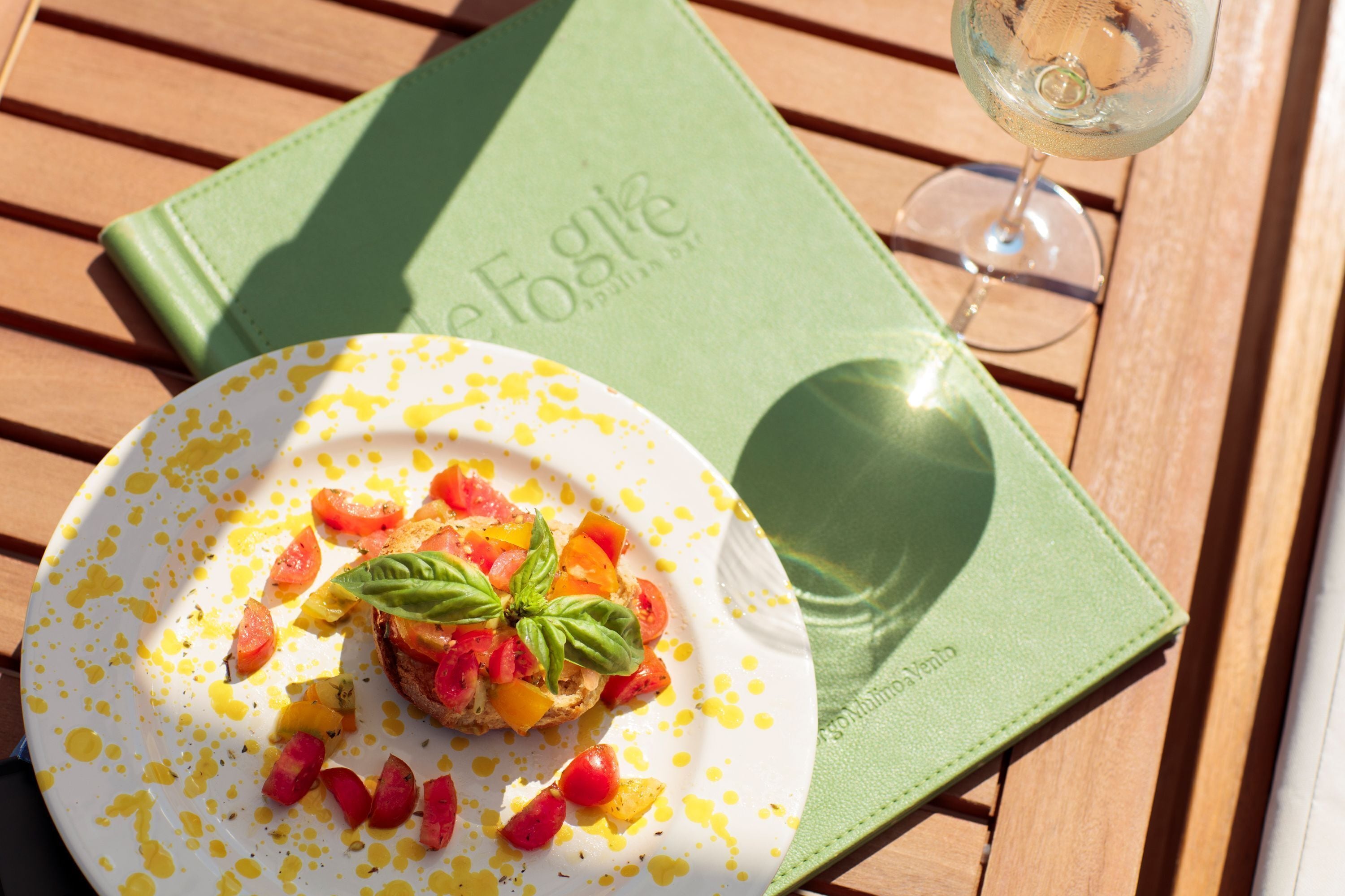 Une assiette de nourriture, un verre de vin blanc et un livre vert sur une table en bois.