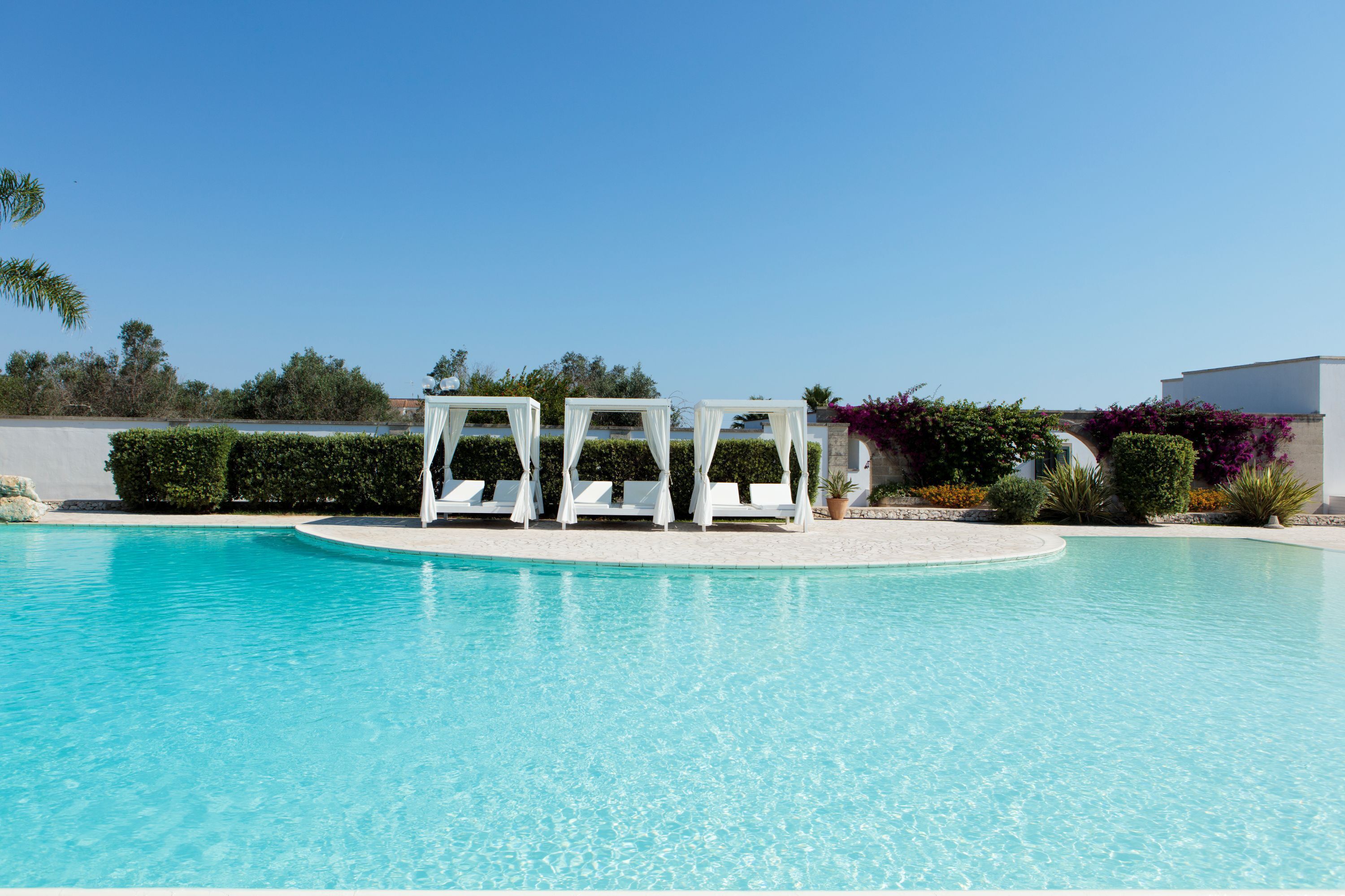 A clear blue pool with white lounge chairs and a white building in the background.