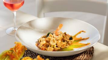 Un plato blanco con un plato de mariscos, un vaso de bebida rosada y un camino de mesa tejido.