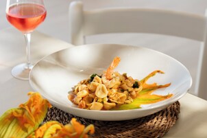 Un plato blanco con un plato de mariscos, un vaso de bebida rosada y un camino de mesa tejido.