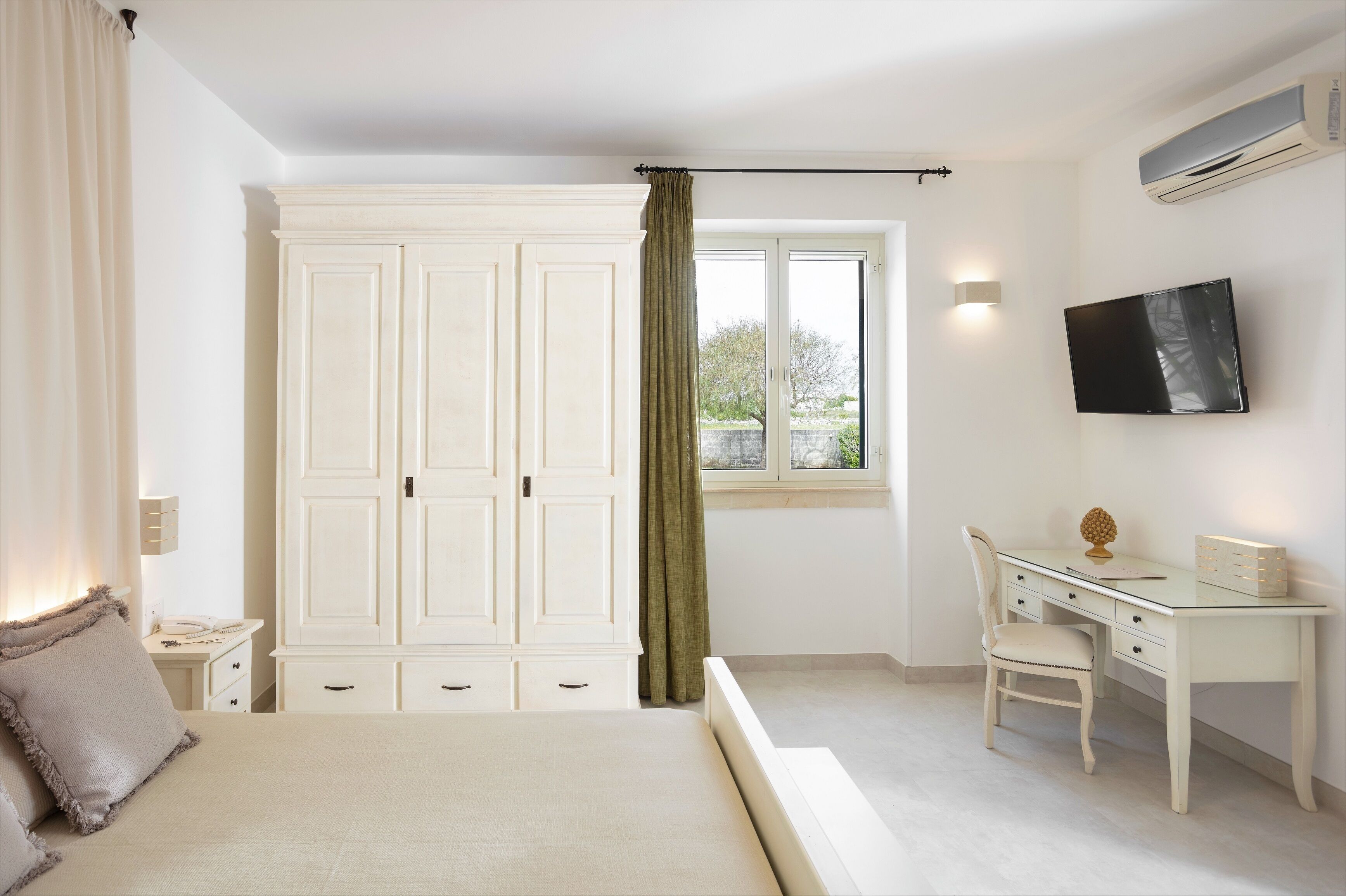 A bedroom with a bed, a desk, a chair, a wardrobe, a TV, and a window with curtains.