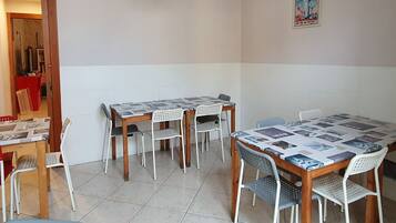 A dining area with a wooden table and white chairs, a tiled floor, and a wall-mounted light fixture.