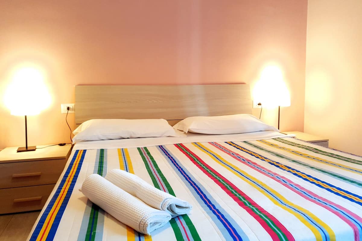 A hotel room with a bed, two bedside lamps, a nightstand, and a striped bedspread.