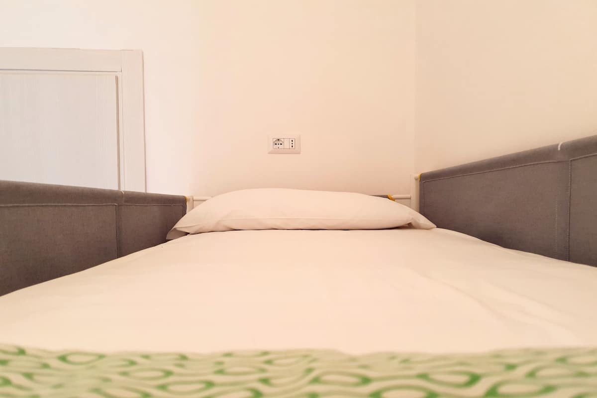 A single bed with a white mattress and a green patterned blanket.