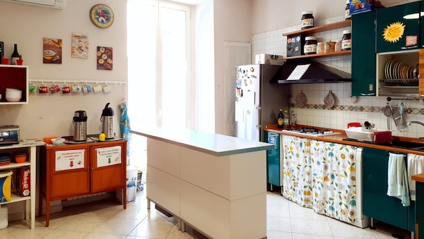 Une cuisine équipée d’un réfrigérateur, d’une cuisinière et de divers appareils de cuisine. Une fenêtre laisse entrer la lumière naturelle, et la cuisine est dotée d’un pare-feu en carrelage et de meubles de rangement en bois.