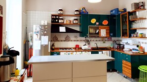 Une cuisine avec un plan de travail blanc, un évier et divers appareils de cuisine. On y trouve des étagères avec des bocaux et une fenêtre au-dessus du plan de travail.