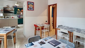 Un espace repas avec des tables et des chaises, une cuisine à l’arrière-plan et une affiche accrochée au mur.
