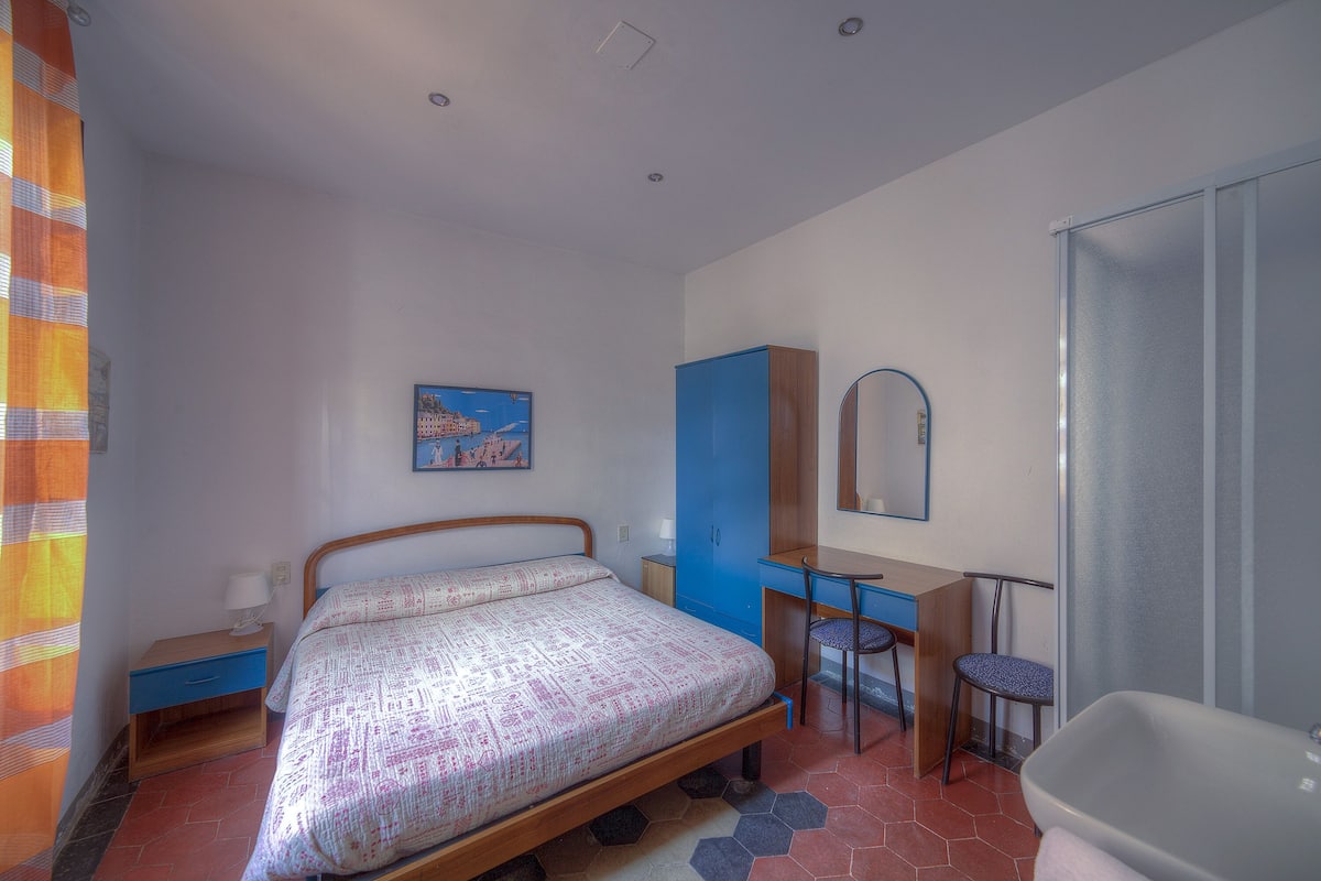 A bedroom with a bed, desk, chair, and a bathroom with a bathtub.