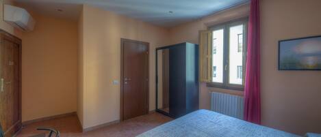 A bedroom with a bed, a wardrobe, a radiator, and a window with curtains.