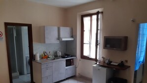 Cocina compacta con lavamanos, estufa y armarios. Se ve una ventana con cortinas, un refrigerador pequeño y un microondas.