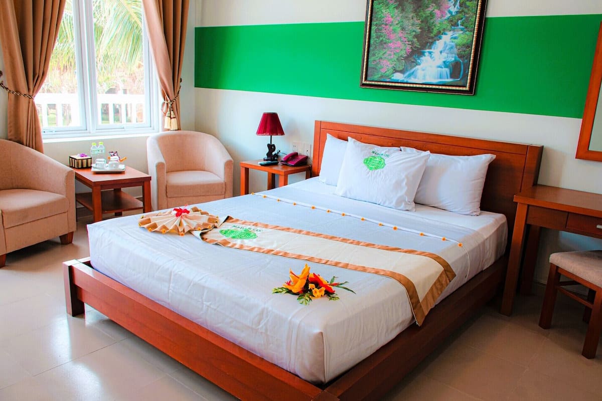 A hotel room with a bed, two chairs, a nightstand, a lamp, and a painting on the wall.
