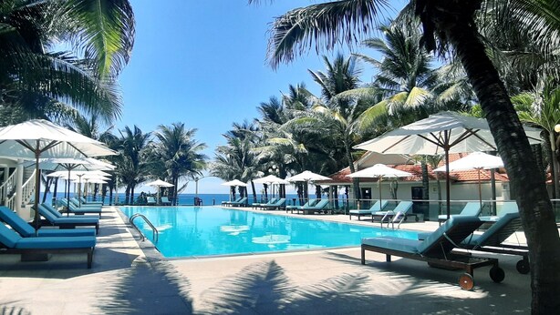 A pool area with lounge chairs and umbrellas, surrounded by palm trees and a clear view of the ocean. - Saigon Emerald Resort (Mui Ne)