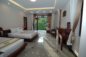 A hotel room with a bed, bedside table, and a view of greenery outside.