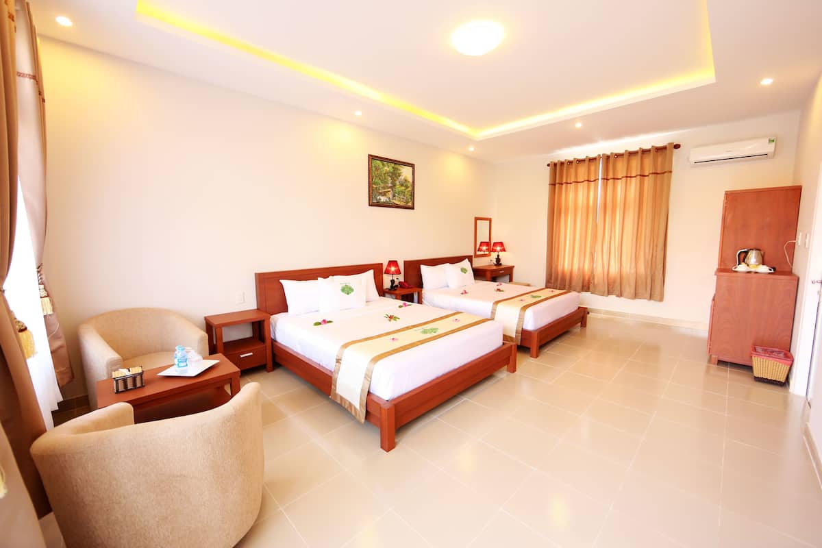 A hotel room with two beds, a chair, a small table, an air conditioning unit, and a cabinet.
