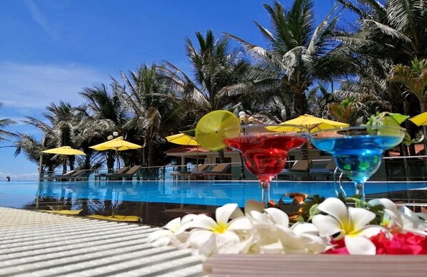 A poolside area with a clear view of the pool, surrounded by palm trees and yellow umbrellas.
