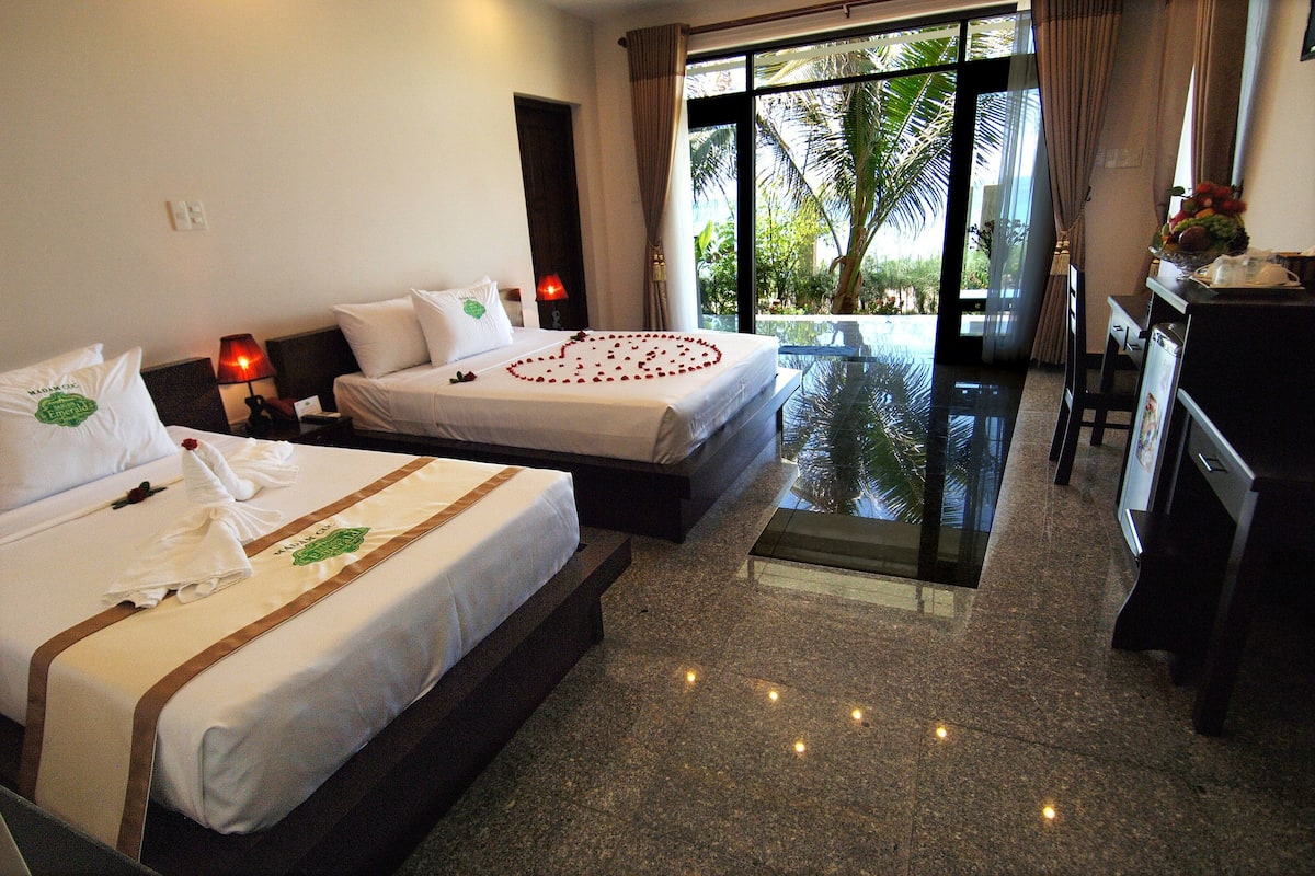 A hotel room with two beds, a desk, and a view of a pool and palm trees.
