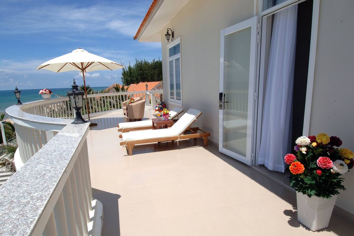 A balcony with two sun loungers, a potted plant with flowers, and a view of the sea.