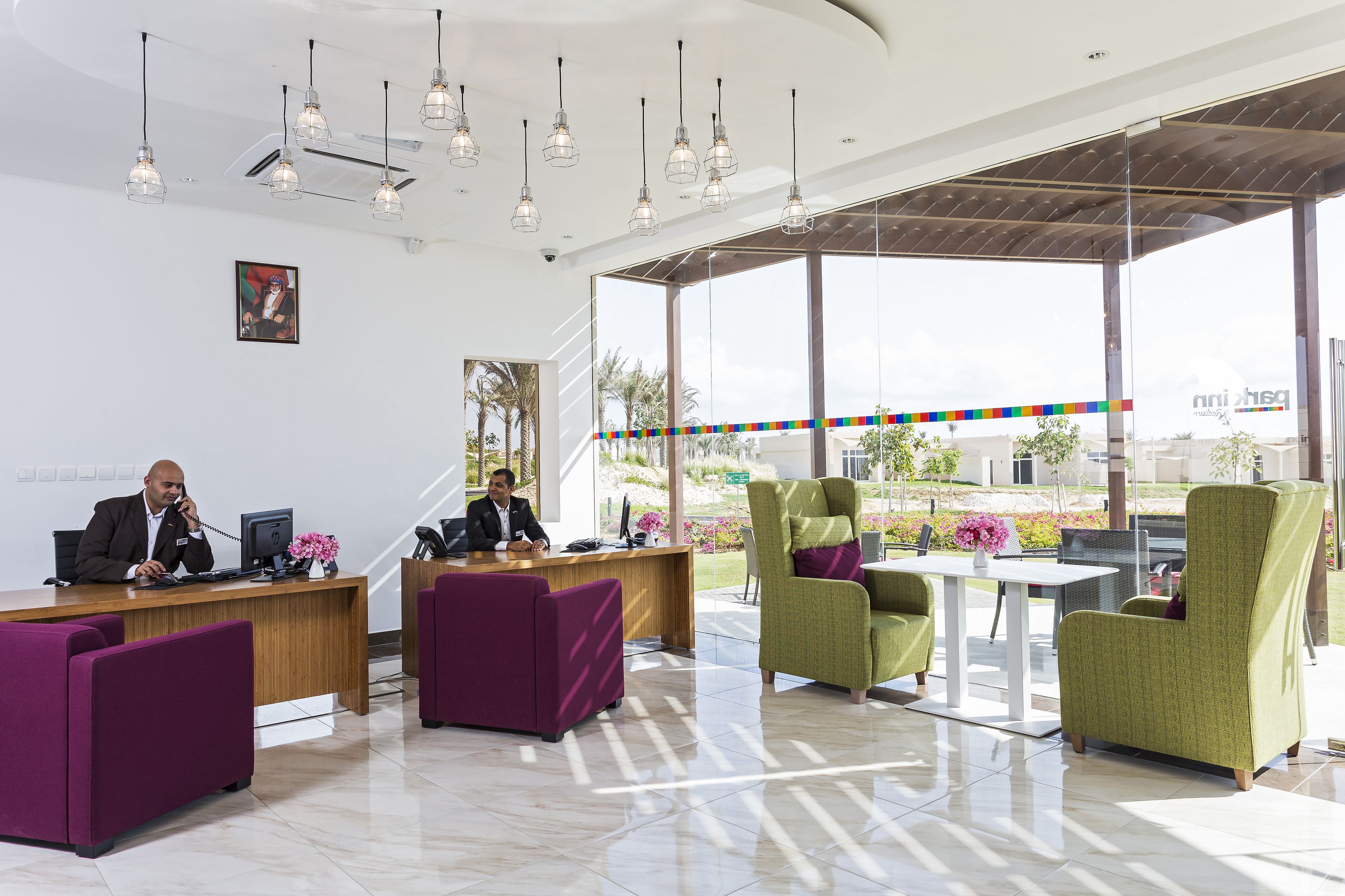 A modern reception area with a wooden desk, purple and green seating, and pendant lighting.