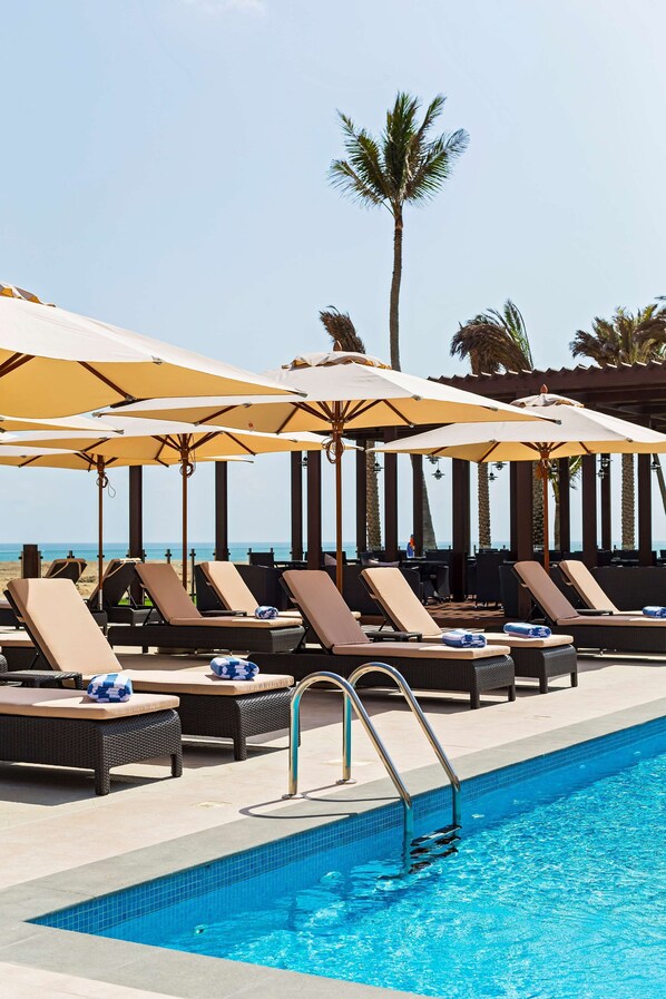 A poolside area with lounge chairs and umbrellas, a pool, and a view of the ocean.