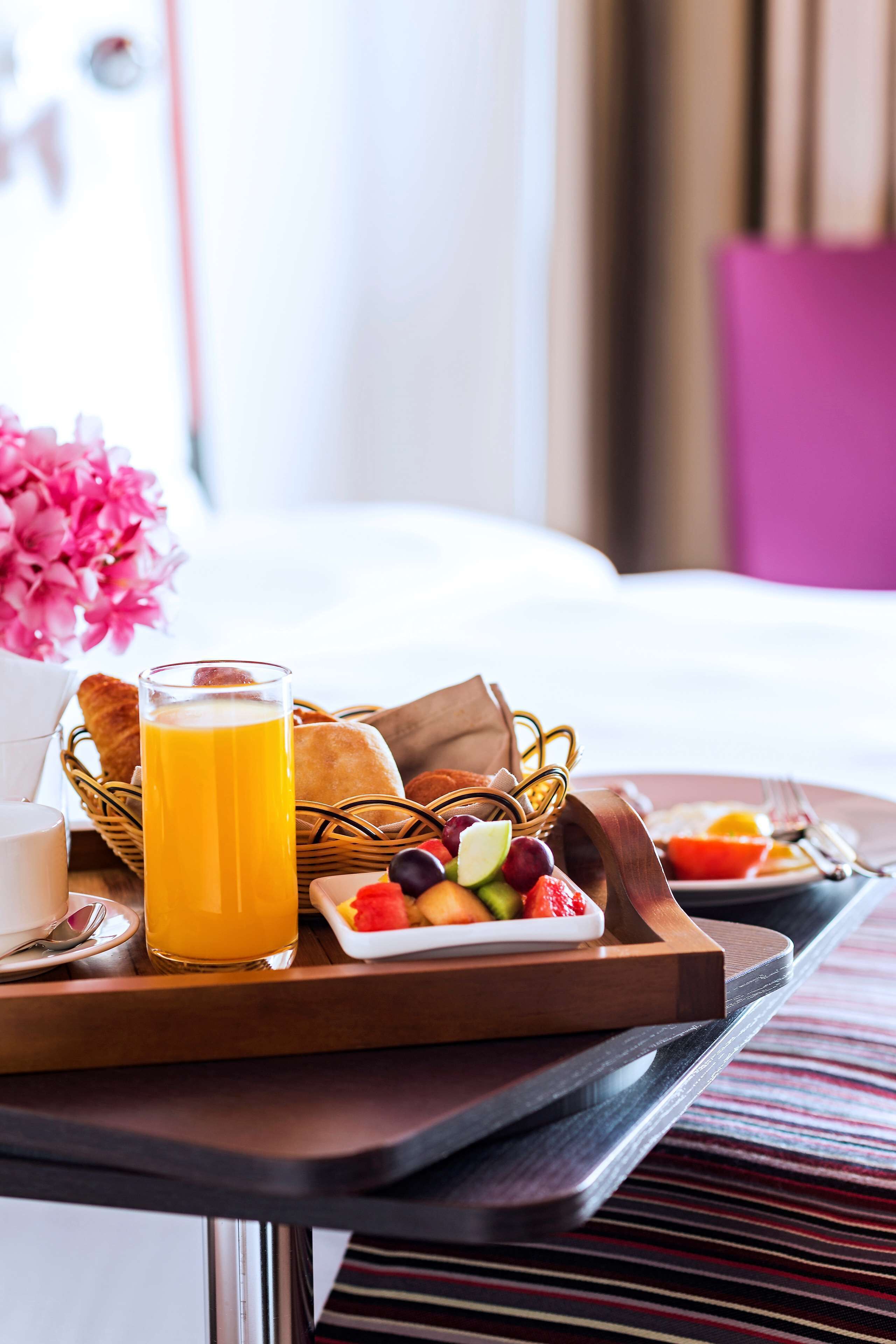 Ein Frühstücksbrett mit Orangensaft, Brot und Obst auf einem Holztisch im Hotelzimmer.